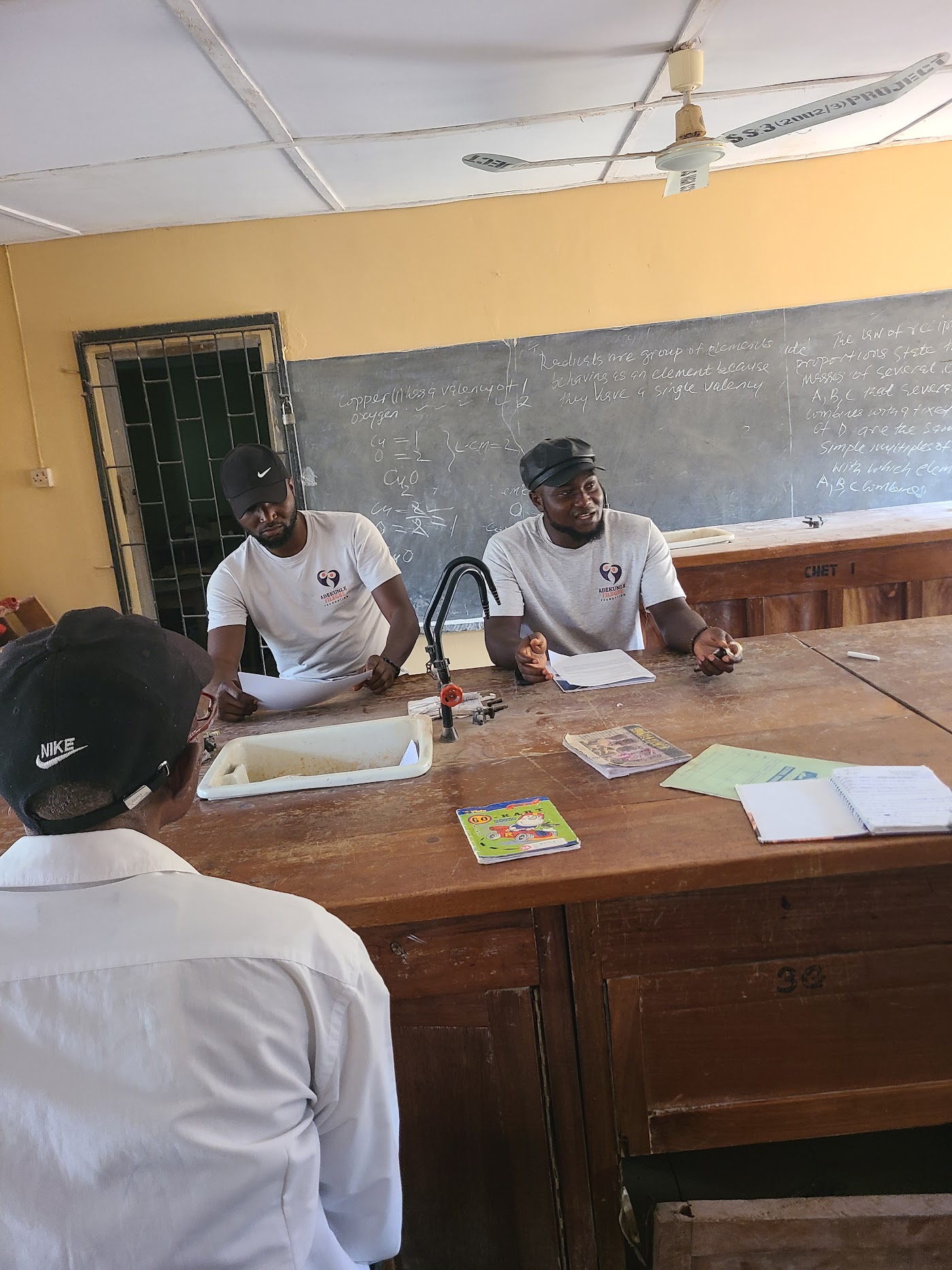 Foundation volunteers talking with a teacher beside a chalkboard.